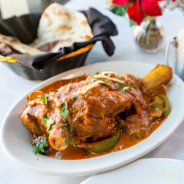 Indian Oven's lamb shank in a rich red sauce with green peppers, garnished with cilantro and ginger.