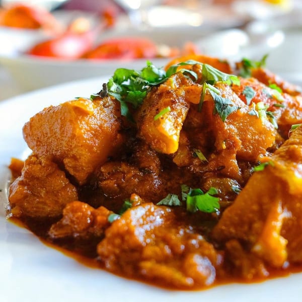 Close-up of Indian Oven's chicken curry with cilantro on a white plate.