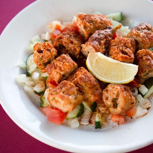 Indian Oven's chicken tikka pieces with chopped onions, cucumbers, tomatoes, and a lemon wedge.
