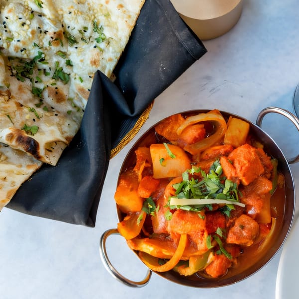 Overhead view of Indian Oven's chicken tikka masala with naan bread on a white table.