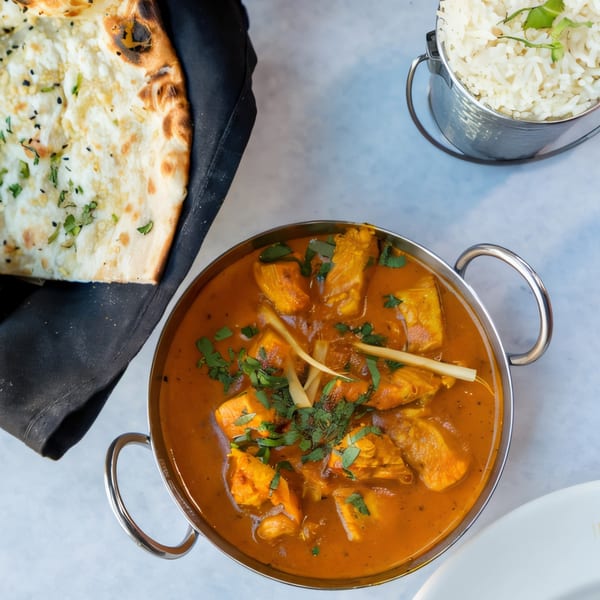 Indian Oven's chicken curry in a metal bowl, with naan bread and rice on the side.