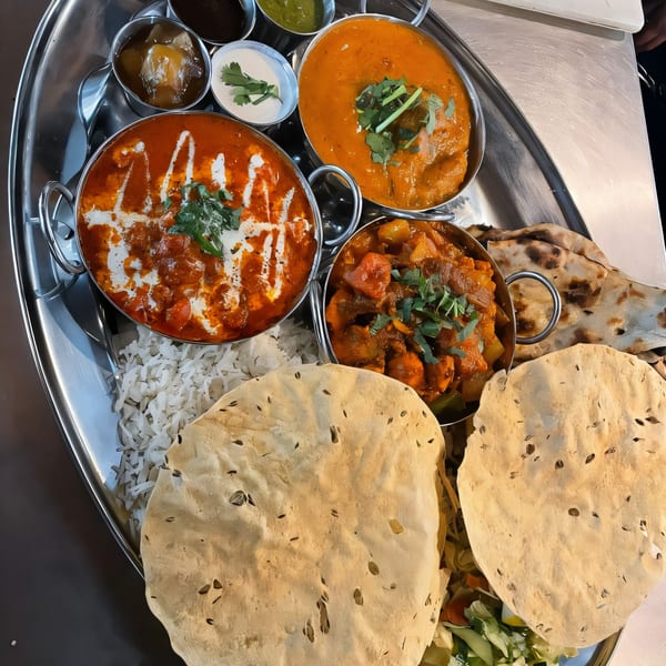 An Indian thali platter with various curries, rice, naan, papadum, and chutneys on a metal tray.