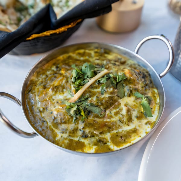 Indian Oven's creamy green Dal Makhani, garnished with cilantro and ginger, in a metal serving bowl.