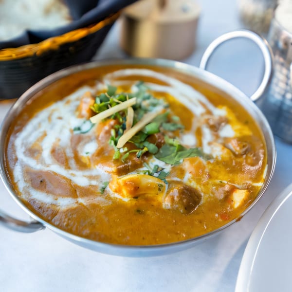 A close-up of Indian Oven's creamy Indian curry, garnished with fresh herbs and ginger, in a metal bowl.